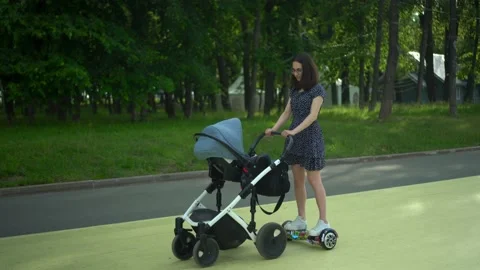 A young woman walks with a stroller on a hoverboard. A modern mother walks with Stock-Footage 204166643