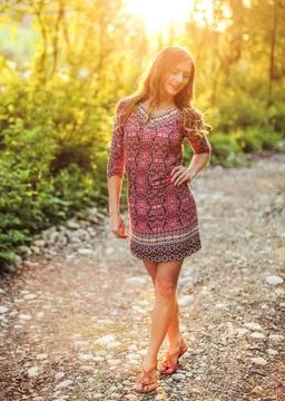 Young woman wearing dress, walking on forest path, eyes half closed, golde... Stock Photos