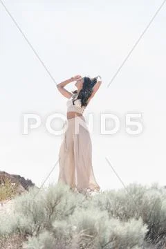 Young woman wearing a long white dress, standing in the prairie. Stock Photos