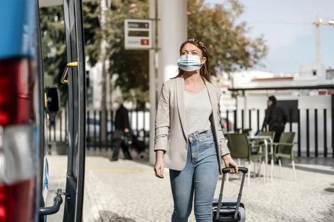 A young woman wearing protective mask boarding the bus with a luggage Stock Photos