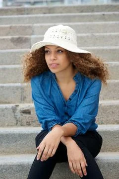 Young woman wearing white hat sitting alone outdoors Stock Photos