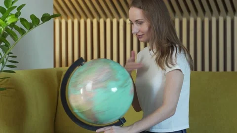 Young woman while sitting on sofa at home holding a world globe choose a route 스톡 동영상 151336818