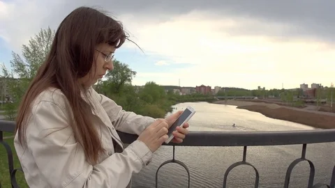 A young woman in a white jacket uses a phone on the city bridge. Stock Footage 76150438