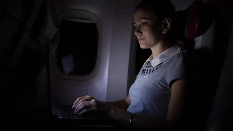 Young woman work on notebook in airplane at night Stock Footage 99394766