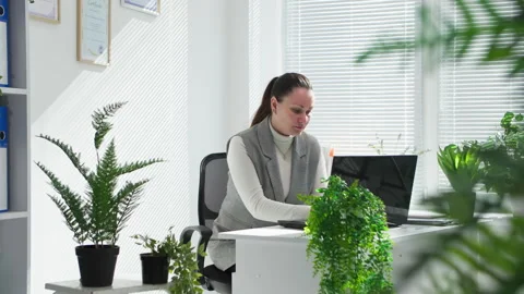Young woman working with documents on computer in office with green plants Stock Footage 306132757