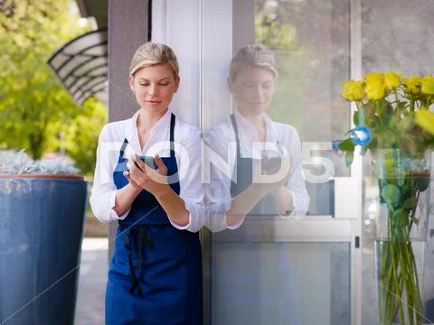 Young woman working as florist in shop and text messaging Stock Photos
