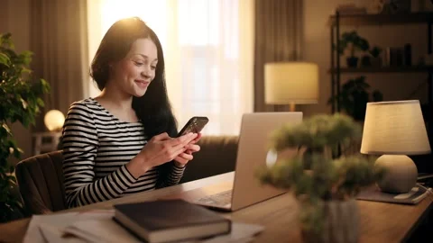 A young woman working on laptop while reading a message on her smartphone. She Stock Footage 312689906