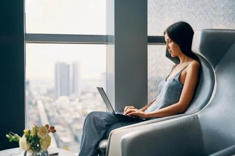 Young woman working on laptop while sitting in a big comfortable chair at modern Stock Photos