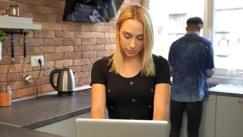 Young woman working at the notebook while boyfriend washes the dishes. Stock Footage 119300016