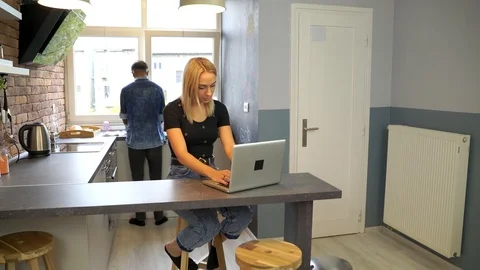 Young woman working at the notebook while boyfriend washes the dishes. Stock Footage 119300072