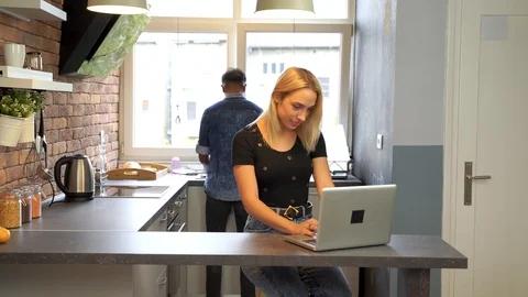 Young woman working at the notebook while boyfriend washes the dishes. Video stock 119300077