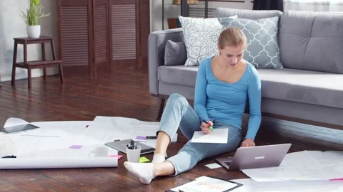 Young woman works with documents using a laptop while sitting on the floor at Stock Footage 169783136