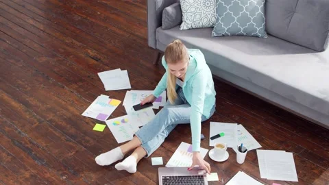 Young woman works with documents using a laptop while sitting on the floor at Stock Footage 169933693