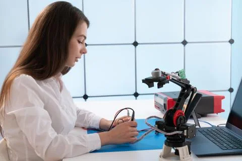 A young woman writes an algorithm for the robot arm. Science Research Laborat Stock Photos