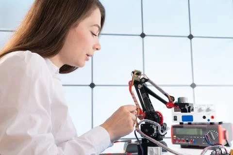 A young woman writes an algorithm for the robot arm. Science Research Laborat Stock Photos