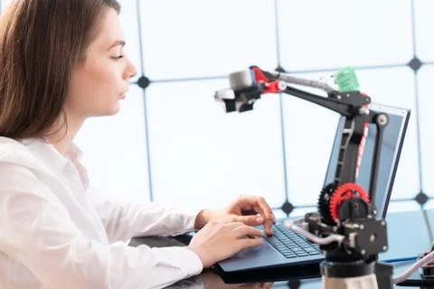 A young woman writes an algorithm for the robot arm. Science Research Laborat Stock Photos