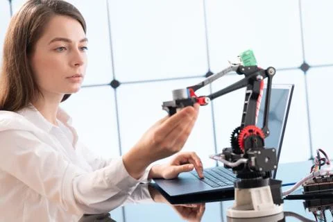 A young woman writes an algorithm for the robot arm. Science Research Laborat Stock Photos