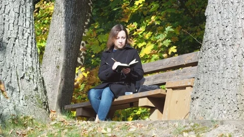 A young woman writes notes in a notebook with a pencil while sitting on a bench Stock Footage 142324327
