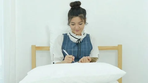 Young woman writing diary while sitting on the bed in her room Stock Footage 81367480