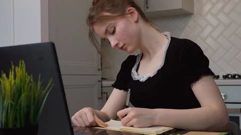 Young woman writing notes while studying on laptop at home Stock Footage 311780110