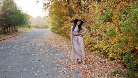 Young woman's elegant and confident walk amidst the leaf-covered walkway Stock Footage 268732968