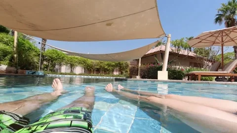 Young women and young man sitting in pool and dangling their feet in water. S Stock Footage