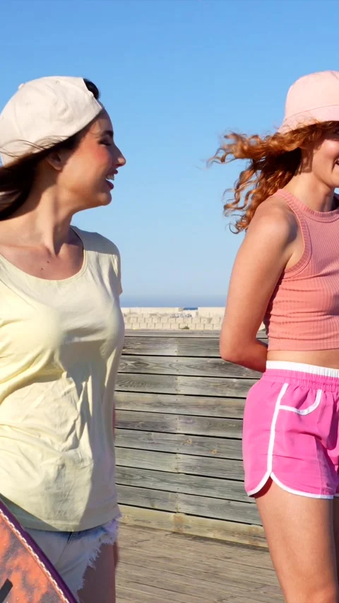 Young women walking and talking on beach boardwalk Stock Footage 309984656