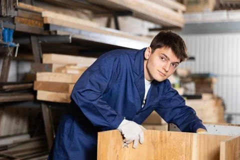 Young worker assembles a wooden table in furniture factory. Work process Stock Photos