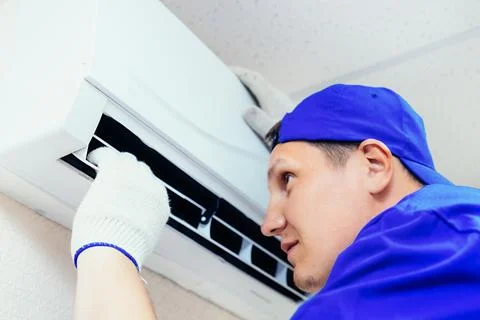A young worker in a blue baseball cap and gloves inspects and maintains the air Stock-Fotos