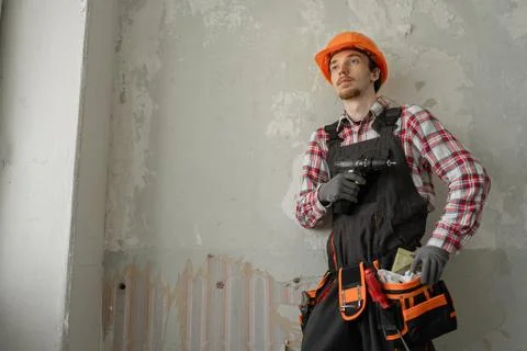 Young worker in hard hat holding perforator or electric drill on wall backg.. Stock Photos