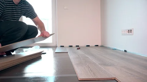 Young worker laying a floor with laminated flooring boards against window light Stock Footage 89407616