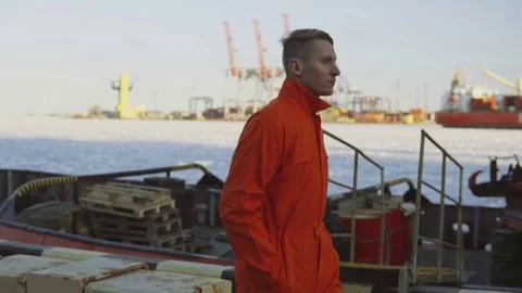 Young worker in orange uniform walking through the harbour by the sea during his Stock Footage 73301247