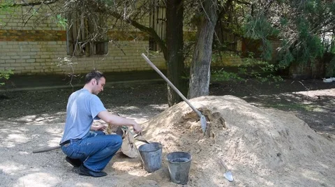 Young worker pours cement from bag in bucket at construction site. Worker squats Stock Footage 64598597
