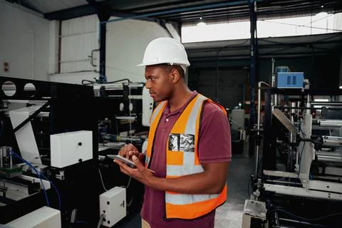 Young worker standing besides machinery holding digital tablet in hand Stock Photos