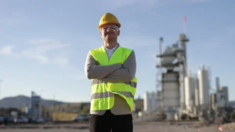 A young worker stands in front of a giant open-air factory. Manufacture of Stock Footage 229358061