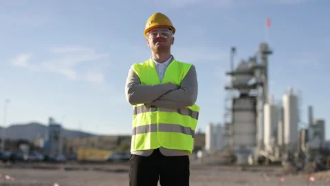 A young worker stands in front of a giant open-air factory. Manufacture of Stock Footage 237930624