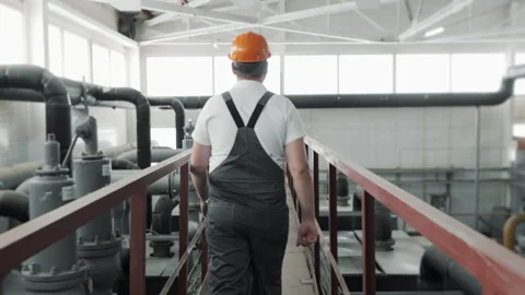 A young worker in a uniform and hard hat, walking through a factory. Stock Footage 306815255