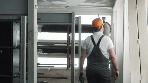 A young worker in a uniform and hard hat, walking through a factory. Stock Footage 306816256