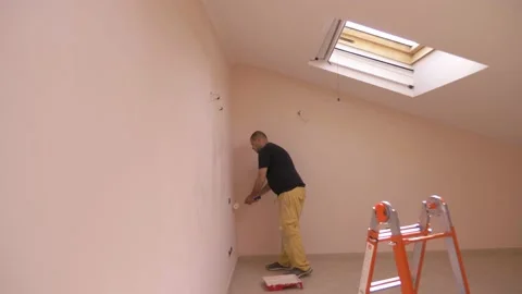 Young worker using the roller brush to paint the walls of the attic Stock Footage 130767390