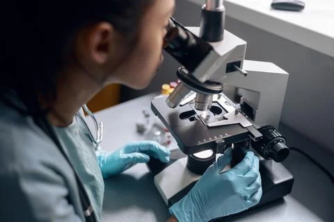 Young worker works with microscope researching material at table in laboratory Stock Photos