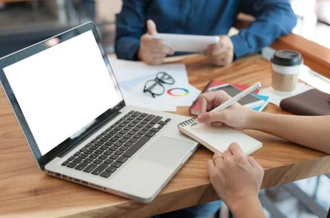 Young worker writing on notebbok while working with colleague Stock Photos