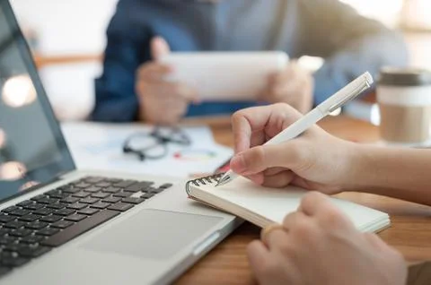 Young worker writing on notebbok while working with colleague Stock Photos
