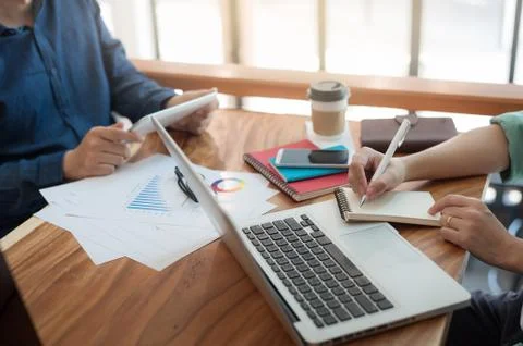 Young worker writing on notebbok while working with colleague Stock Photos