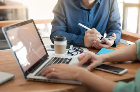 Young worker writing on notebbok while working with colleague Stock Photos