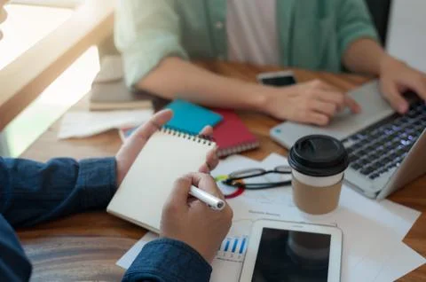 Young worker writing on notebbok while working with colleague Stock Photos