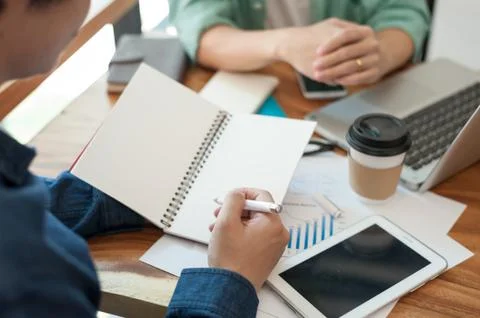 Young worker writing on notebbok while working with colleague Stock Photos