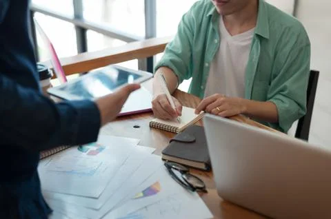 Young worker writing on notebbok while working with colleague Stock Photos