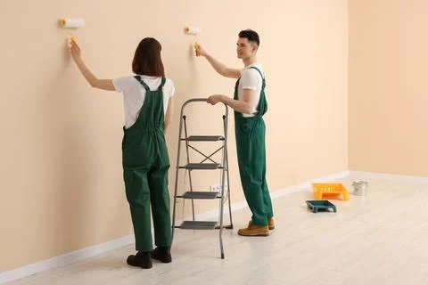 Young workers painting wall with rollers indoors. Room renovation Fotos de archivo
