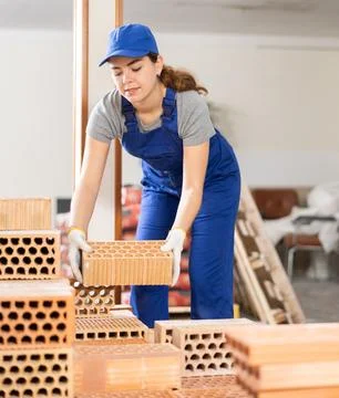 Young workwoman stacking bricks at construction site indoors Stockfoto's
