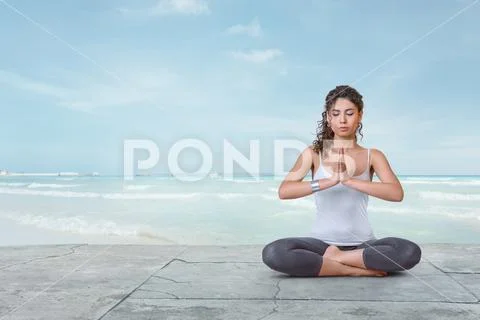 Young yogi woman is meditating on the beach in lotus position Stock Photos